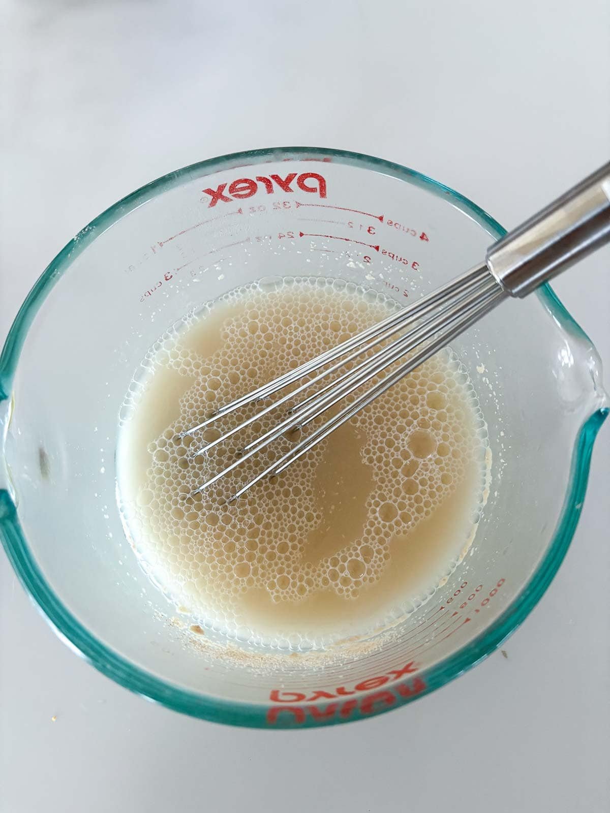 whisk mixing together yeast and warm water in measuring cup.