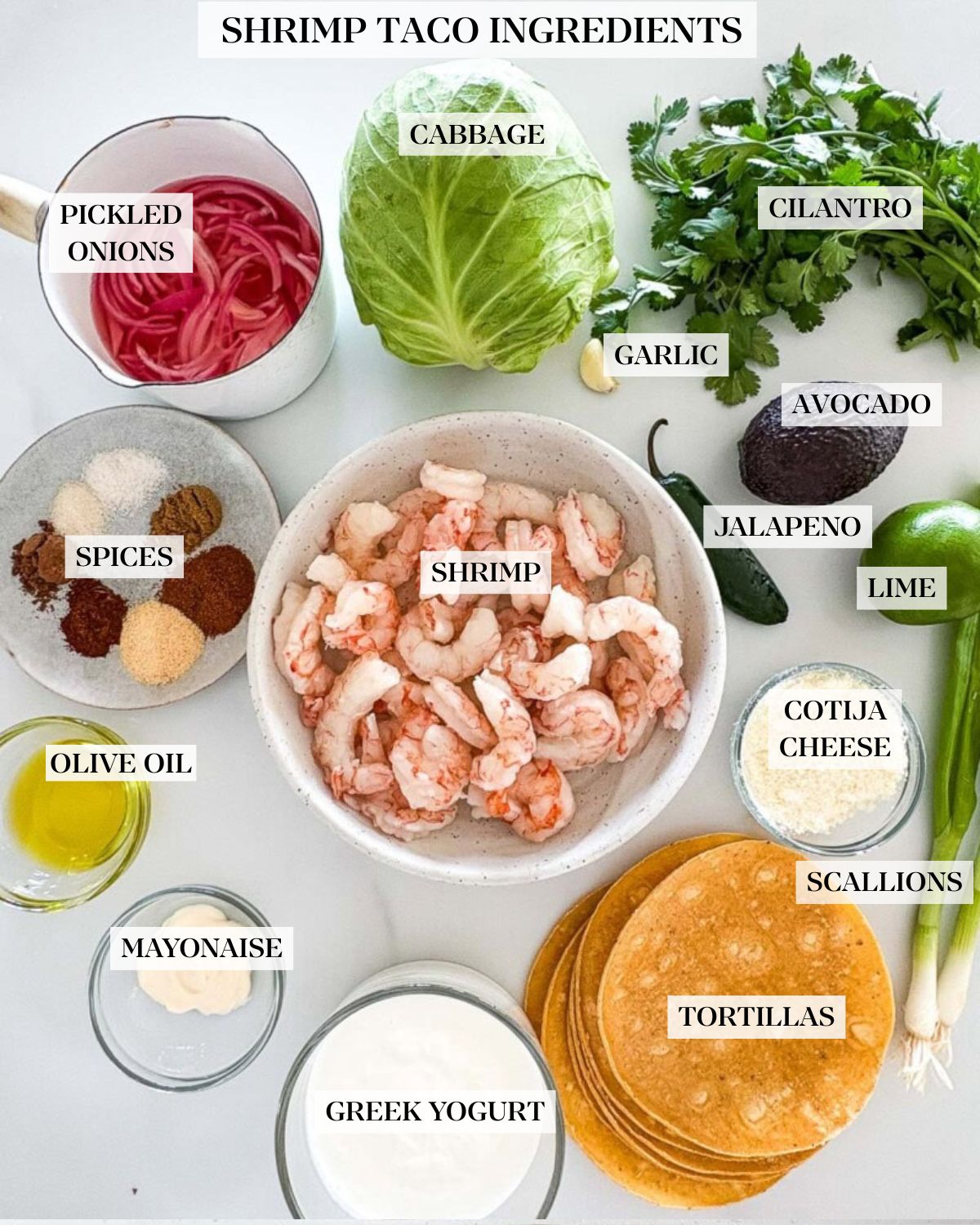 Ingredients arranged neatly on the counter to make shrimp tacos - pot of pickled onions, green cabbage, garlic, cilantro, avocado, jalapeno, lime, green onions, spices, shrimp, oil, mayo, greek yogurt, and tortillas.