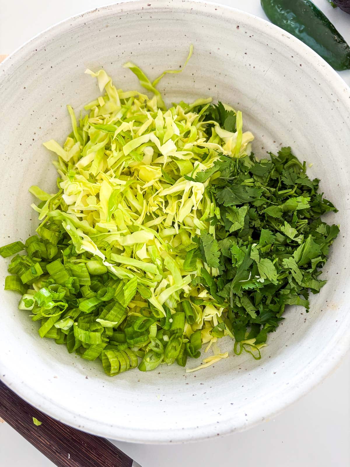 some of the slaw ingredients added to a bowl - cabbage, cilantro, and green onions.