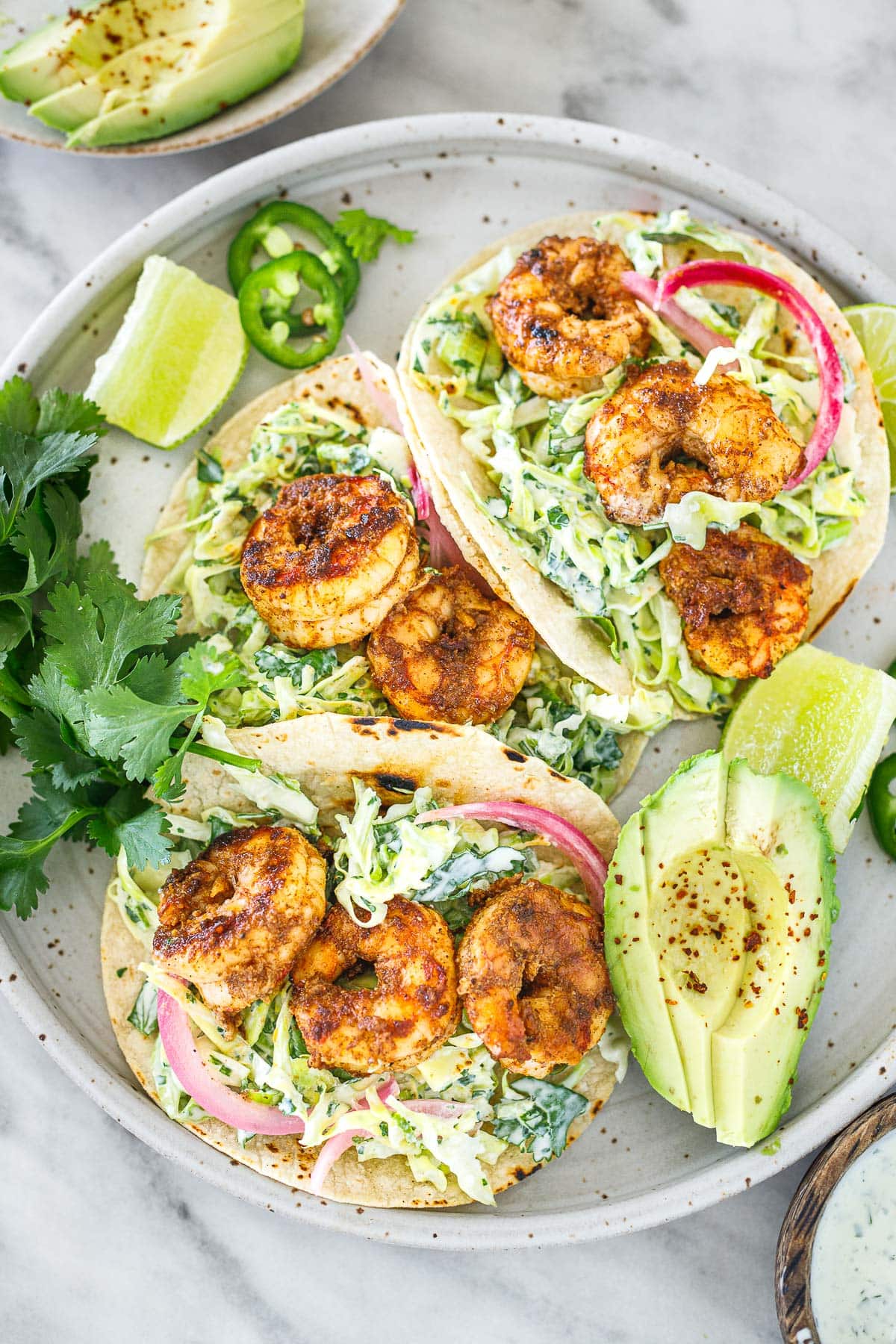 cilantro lime tacos assembled on a plate with avocado, limes, cilantro, and jalapeno slices.