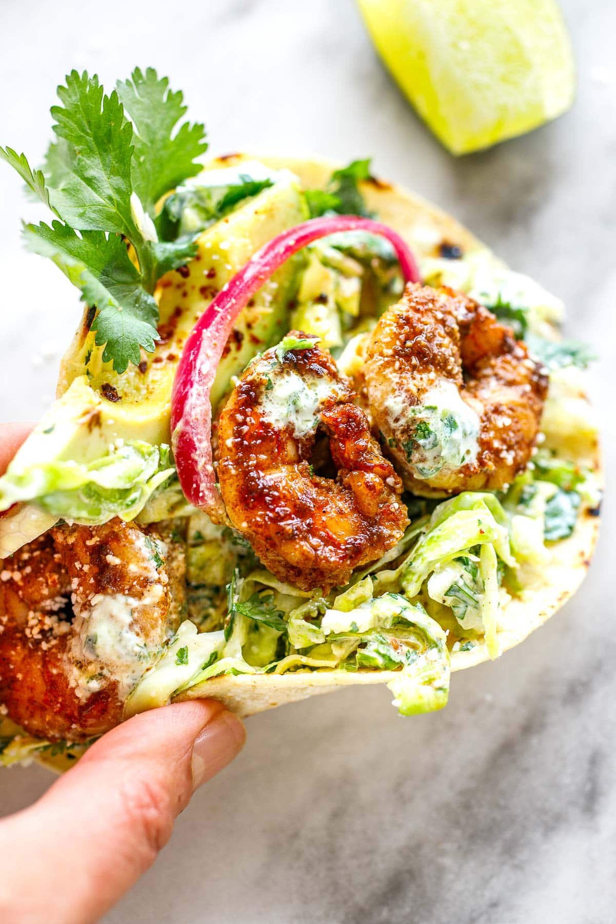 hands holding a shrimp taco with cilantro lime slaw and cilantro lime crema and pickled onions.