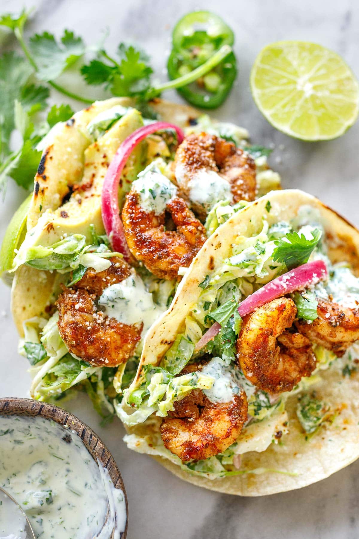 two shrimp tacos with cilantro lime slaw, cilantro lime crema, and pickled red onions.