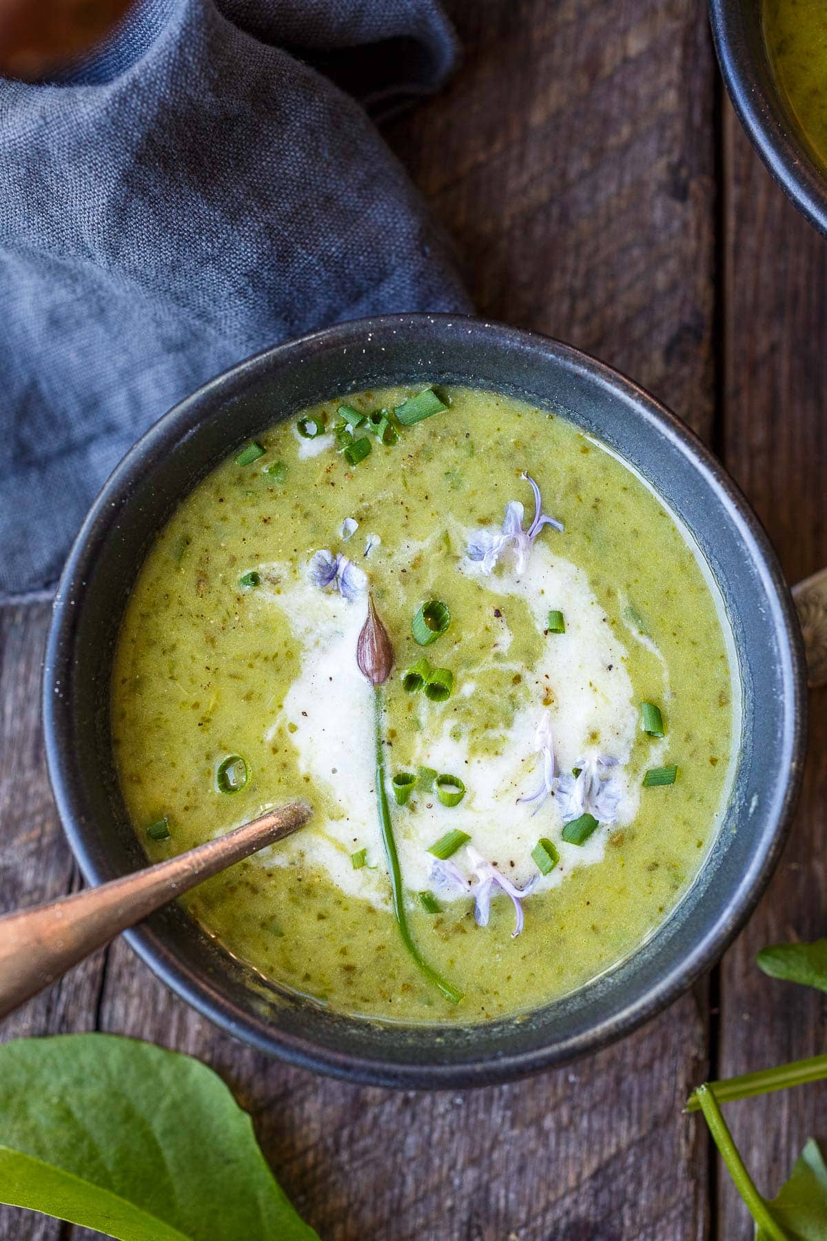 bowl of sorrel soup with a swirl of cream, chive blossom, and scallions on top with spoon.