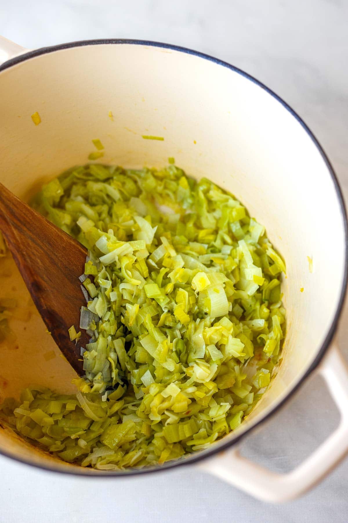dutch oven with sautéed leeks stirred with wooden spoon.