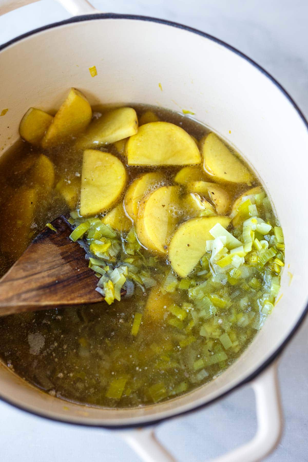 dutch oven with gold potatoes and broth added to the leeks, with wood spoon to stir.