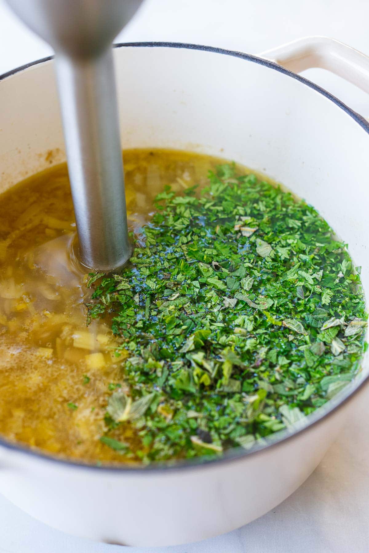 fresh herbs added to pot of sorrel soup with immersion blender to blend soup.