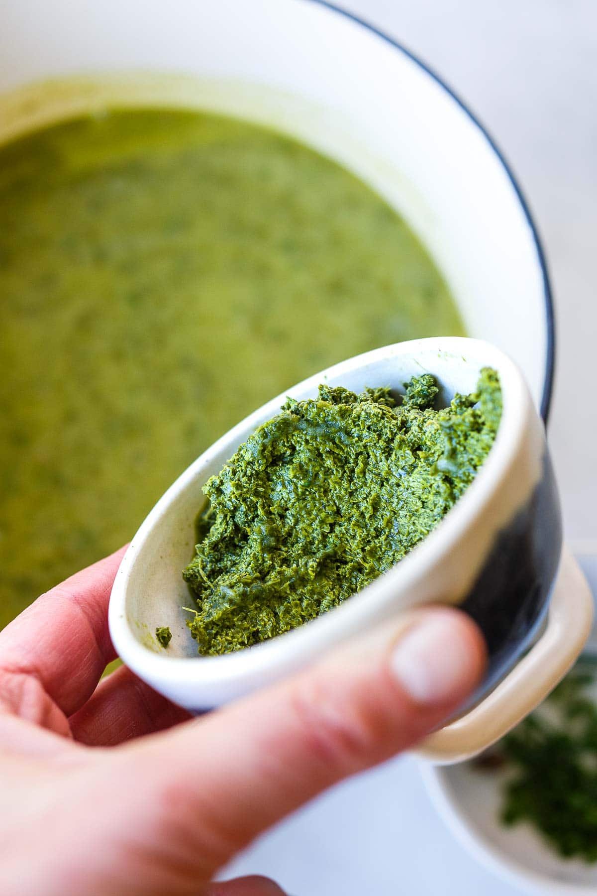 hand holding small bowl of sorrel paste about pot of soup.