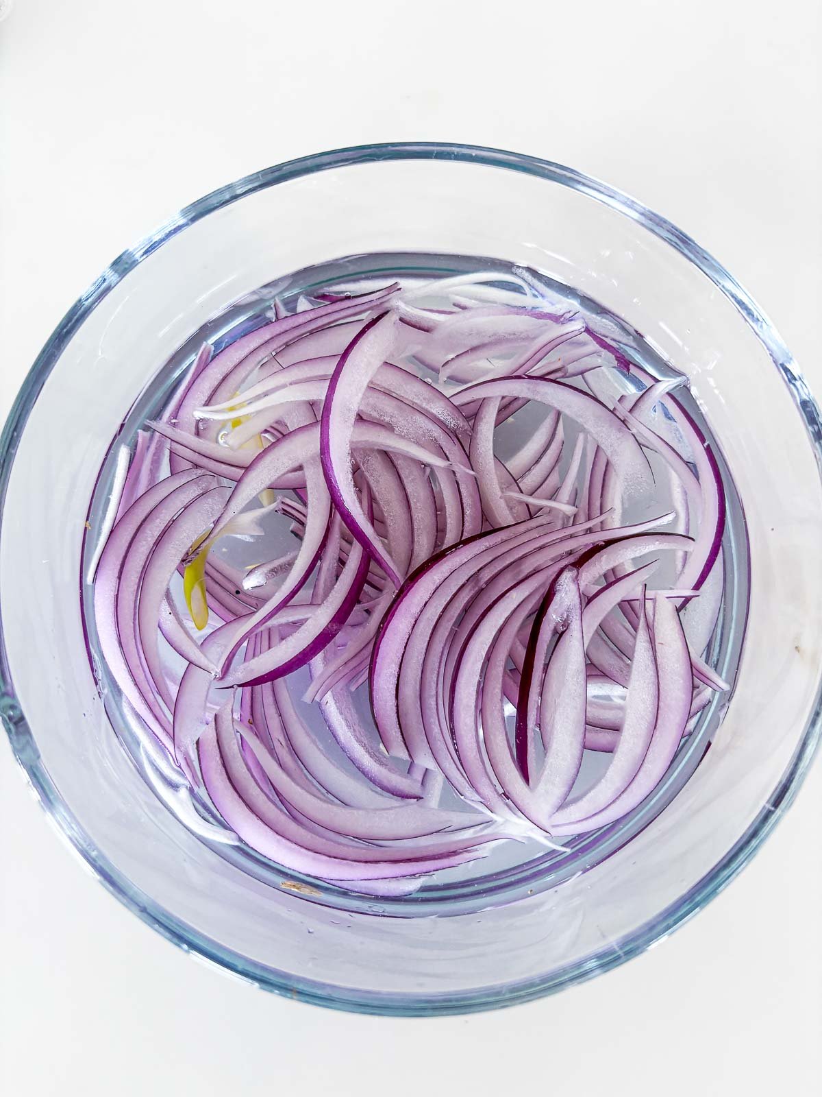 thinly sliced red onions in bowl of salt water.