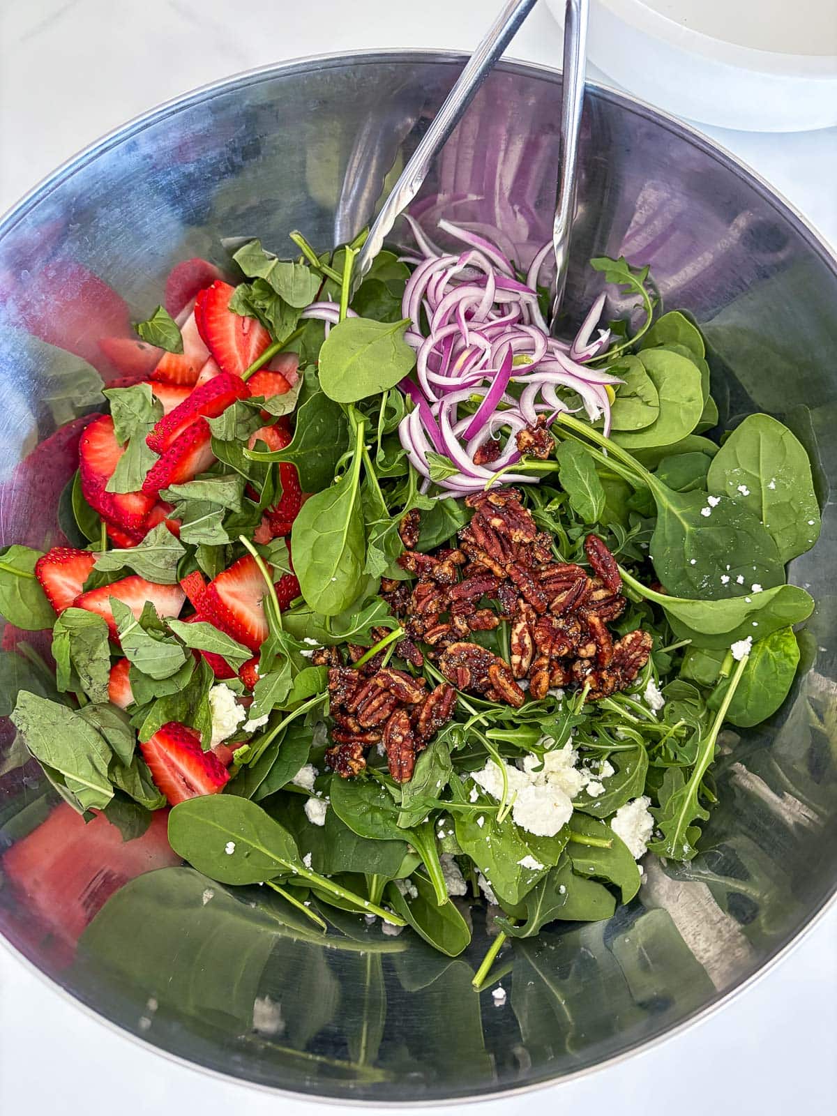 large mixing bowl with strawberry and spinach salad and tongs to mix.