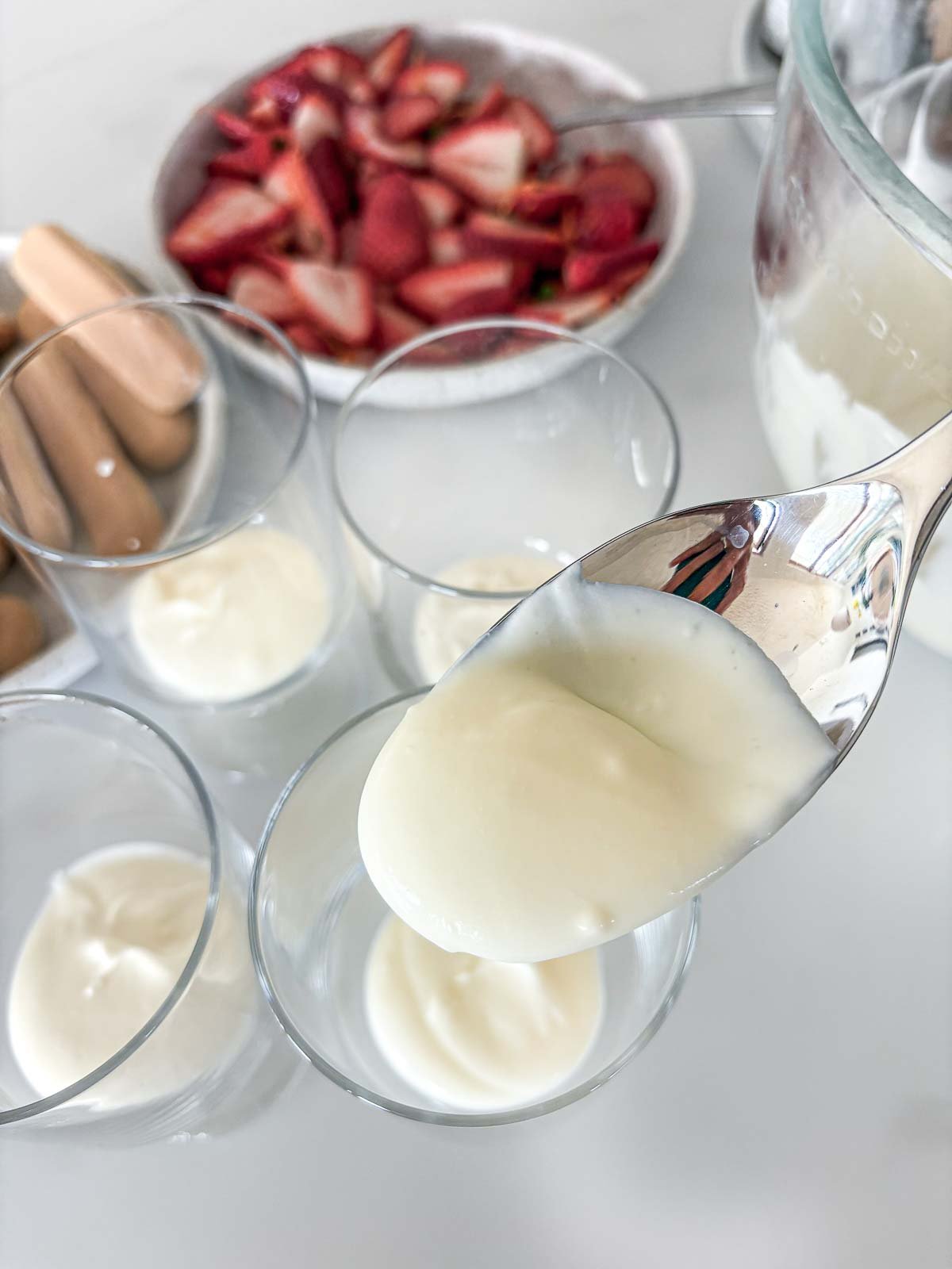 spoon holding up mascarpone mixture and four glasses with the mixture placed in each.