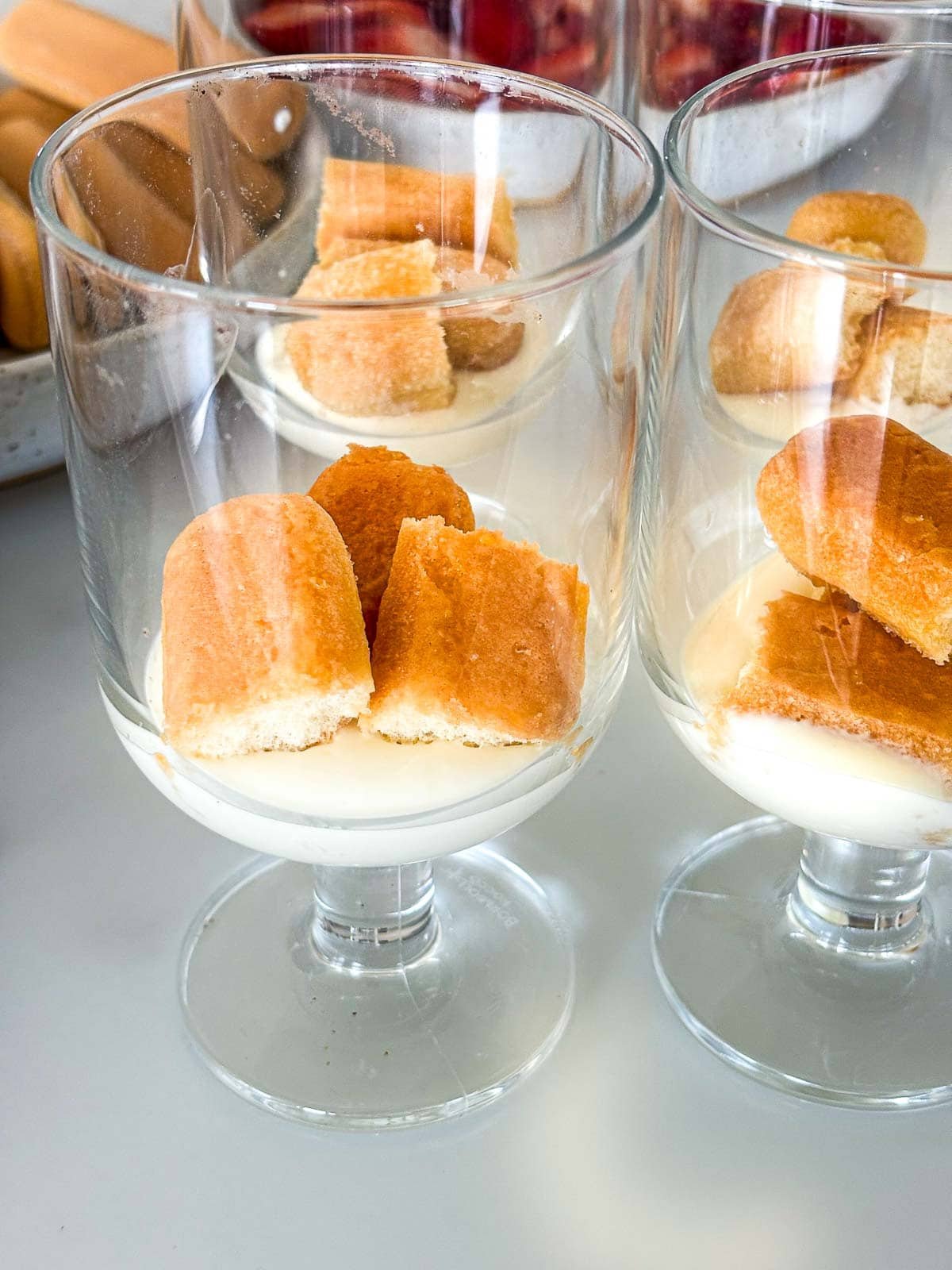 glasses with stems featuring the mascarpone mixture on the bottom and soaked ladyfingers broken into 3 parts layered on top.