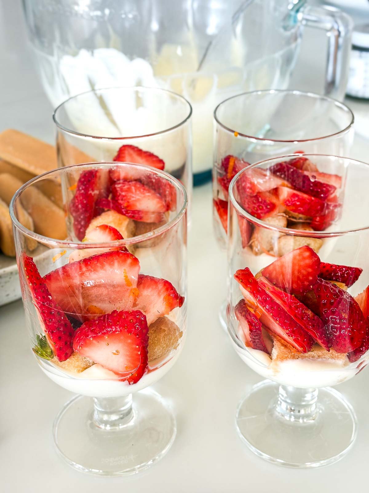 assembling strawberry tiramisu in glasses with macerated sliced strawberries places on top of ladyfingers and mascarpone.