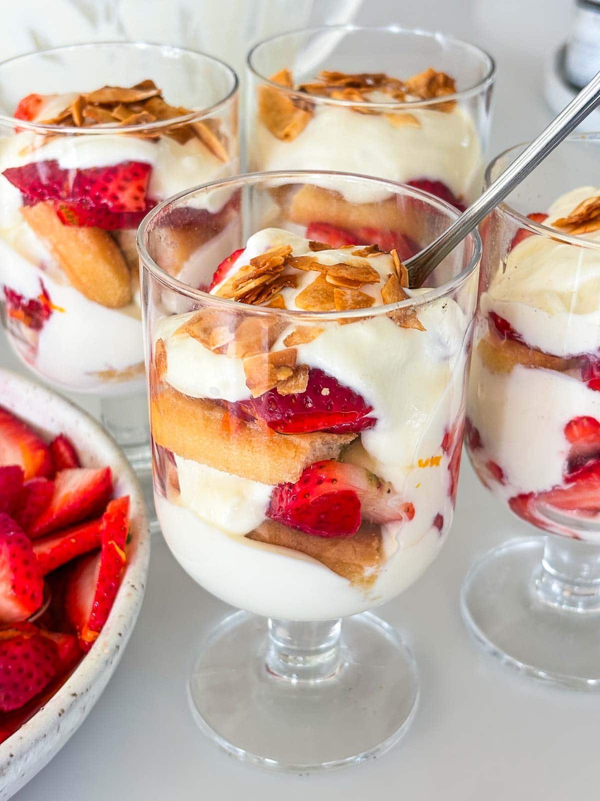 assembled strawberry tiramisu in glasses with toasted coconut on top served with a spoon.
