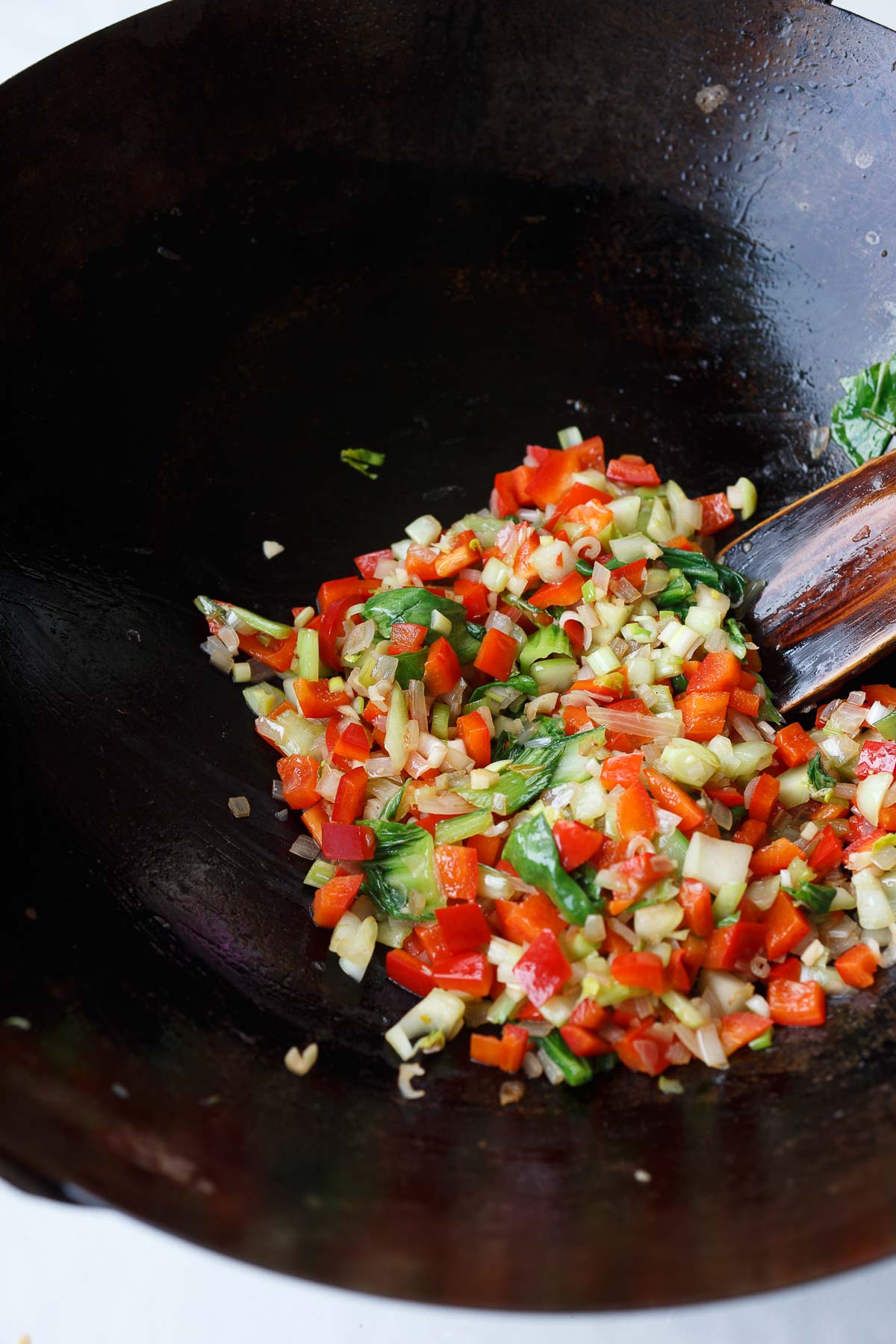 wok with diced veggies stir-frying in oil with a wood spatula. 