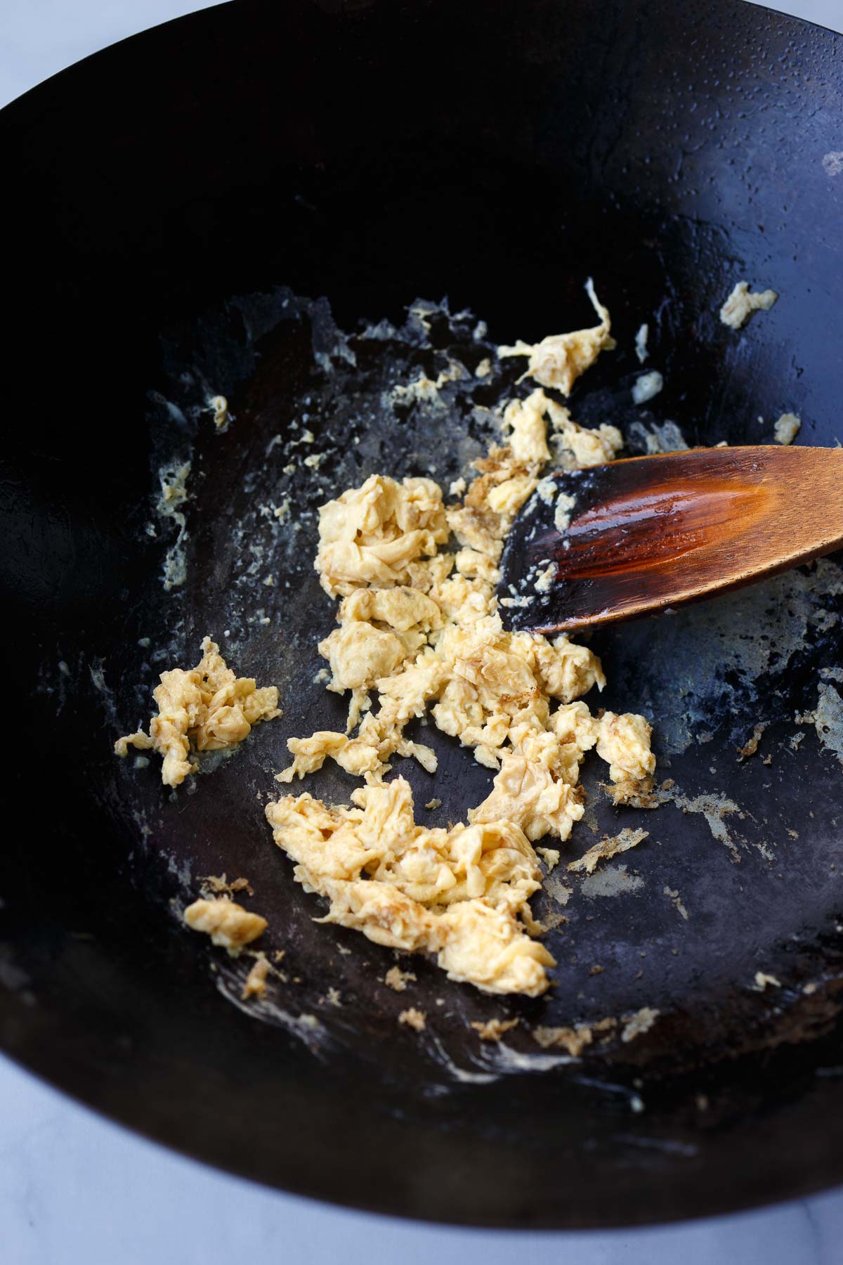 wok with wood spatula stirring scrambled eggs. 