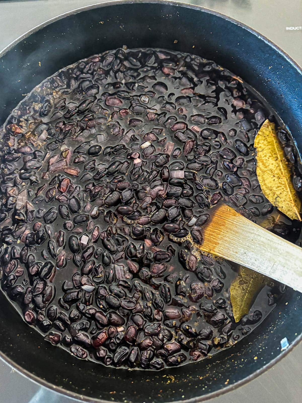 large pot with cooked black beans from scratch, with two bay leaves and a wood spoon.