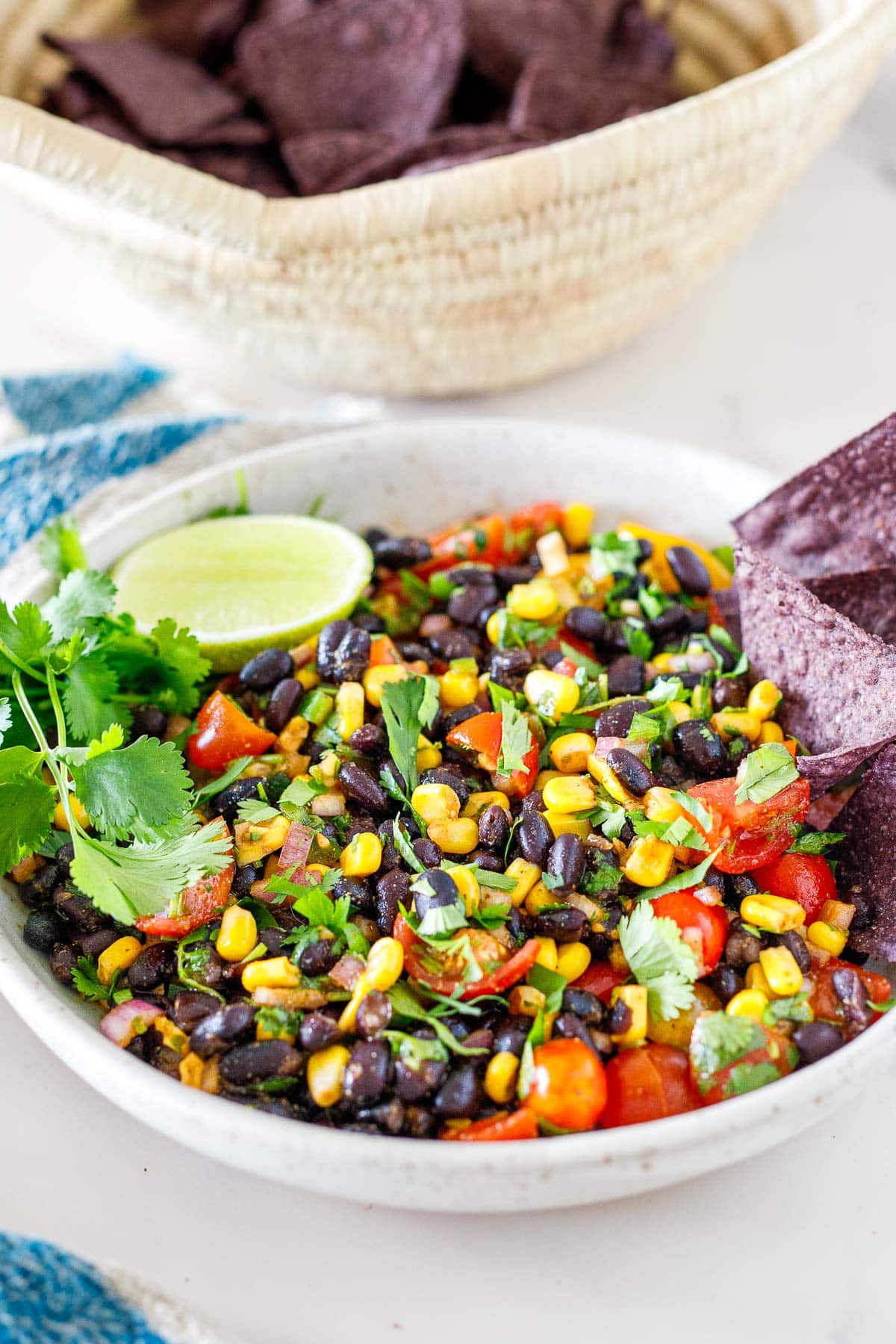 serving bowl with black bean salsa with blue corn chips, fresh cilantro, and lime. 