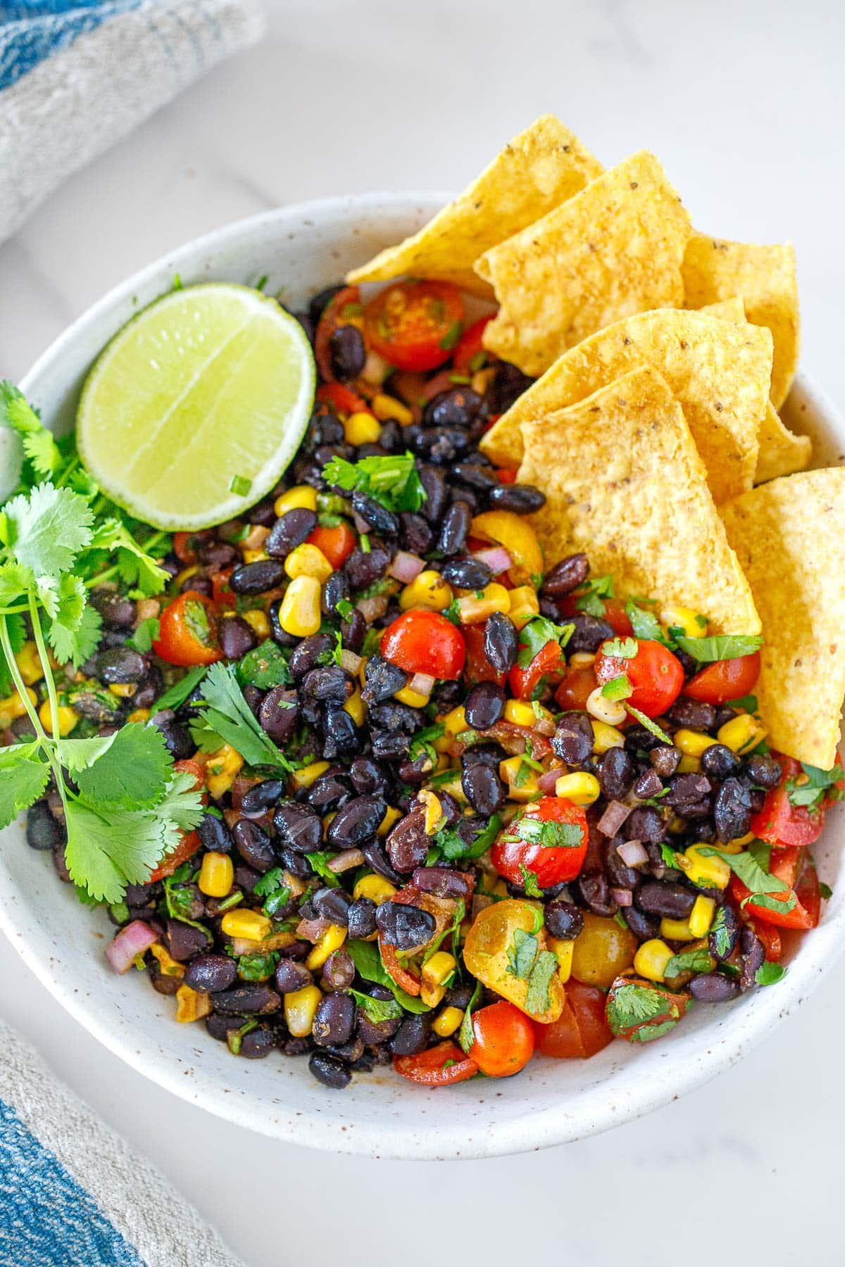 serving bowl with black bean salsa, served with tortilla chips, fresh cilantro, and lime half. 
