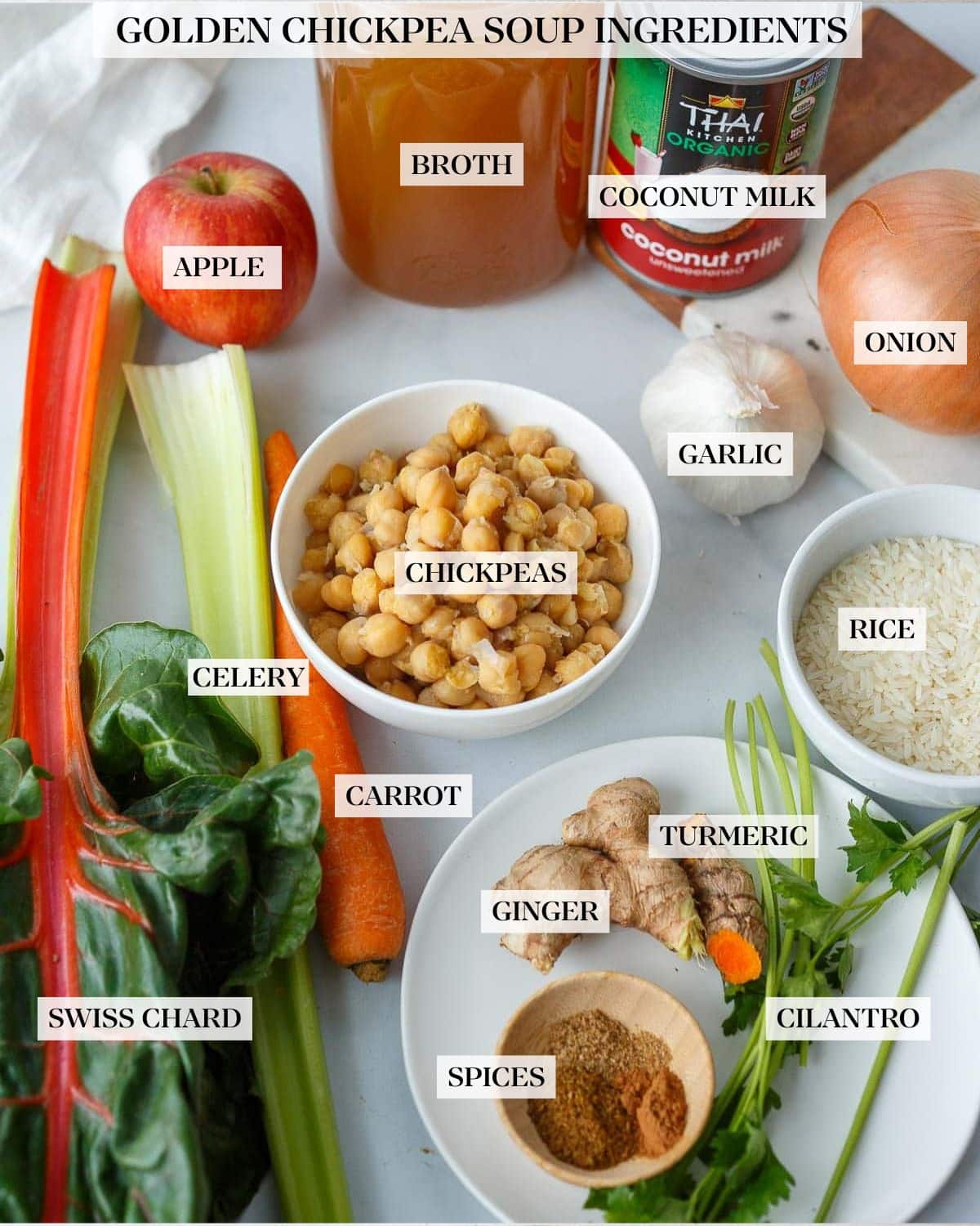 ingredients for creamy chickpea soup laid out - chickpeas, coconut milk, onion, garlic, apple, broth, chard, celery, carrot, rice, turmeric, ginger, spices, parsley.