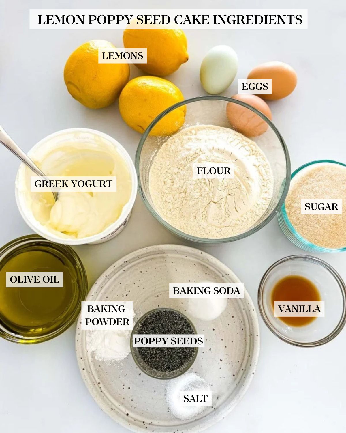 ingredients for lemon poppy seed cake - lemons, eggs, Greek yogurt, flour, sugar, olive oil, vanilla, poppy seeds, baking powder, baking soda, salt, arranged neatly in bowls. 