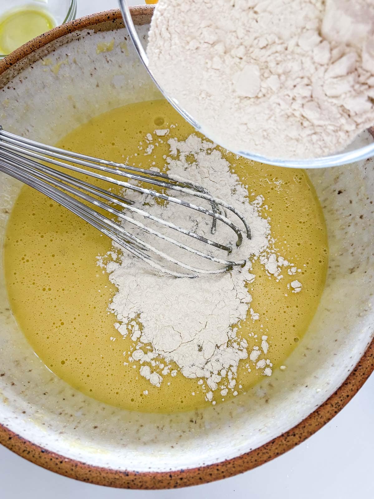 lemon poppy seed cake batter in bowl with whisk mixing flour in. 