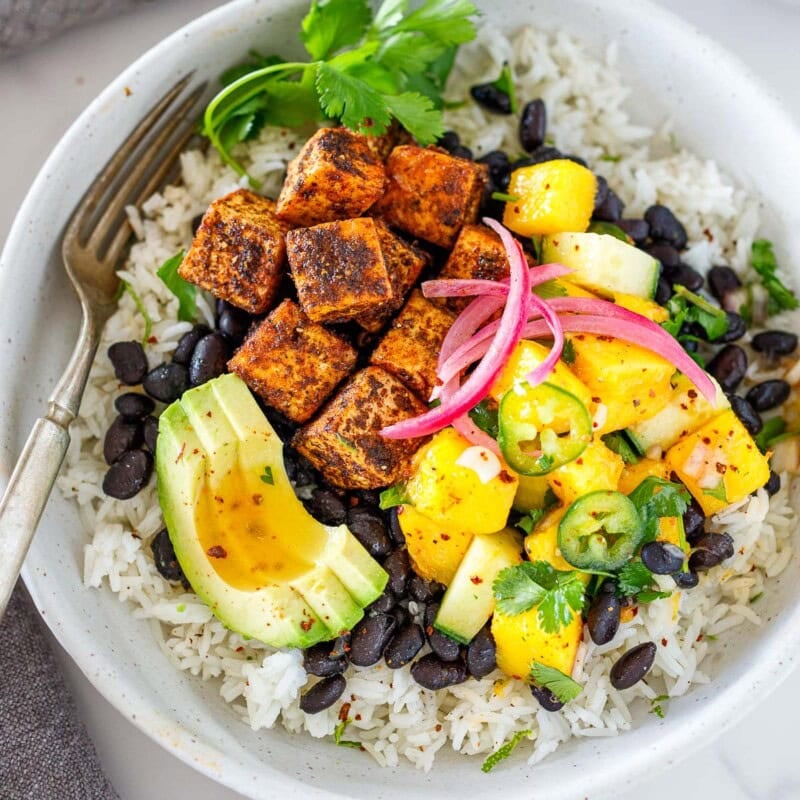 Here is one of my favorite tofu bowl recipes! Spicy jerk tofu served over black beans and rice with a refreshing mango salad, topped with pickled onions and avocado. So much flavor!