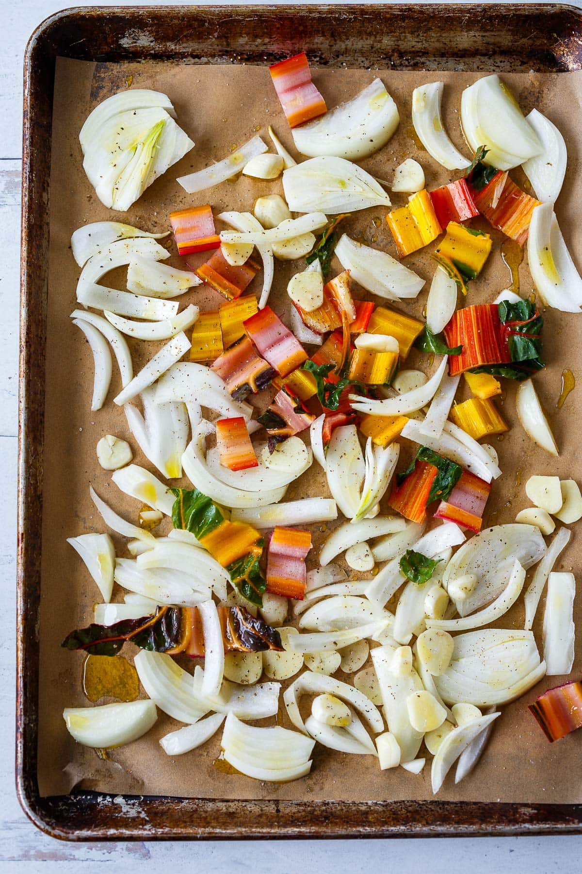 parchment lined sheet pan with onion, chard stems, and garlic. 