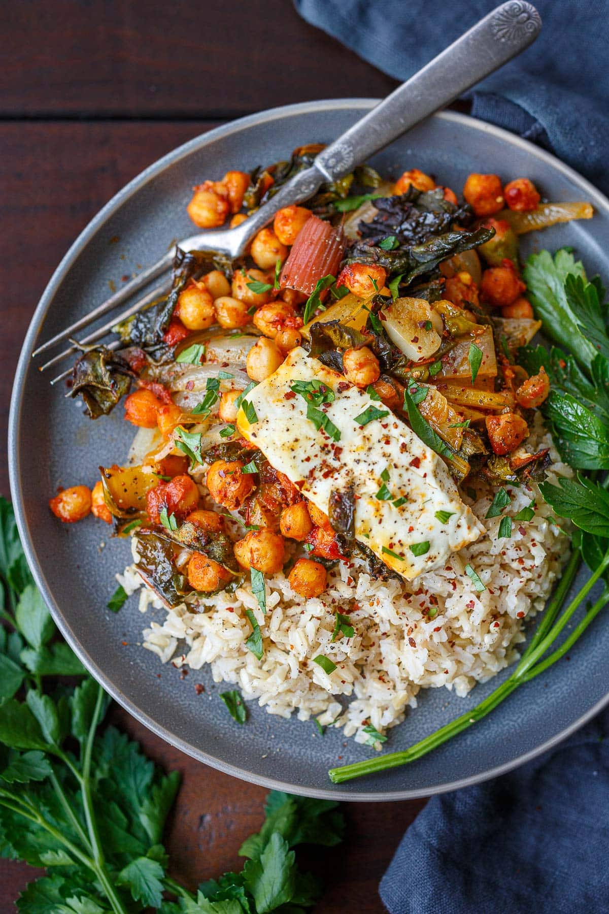 plate with rice, baked feta with chickpeas in harissa sauce with onions and chard, parsley garnish, and fork. 