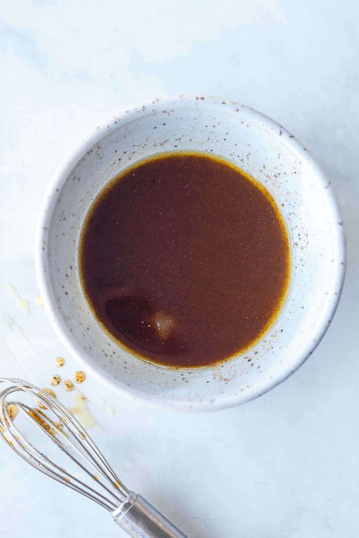 small bowl with cinnamon white balsamic dressing with small silver whisk off to the side.