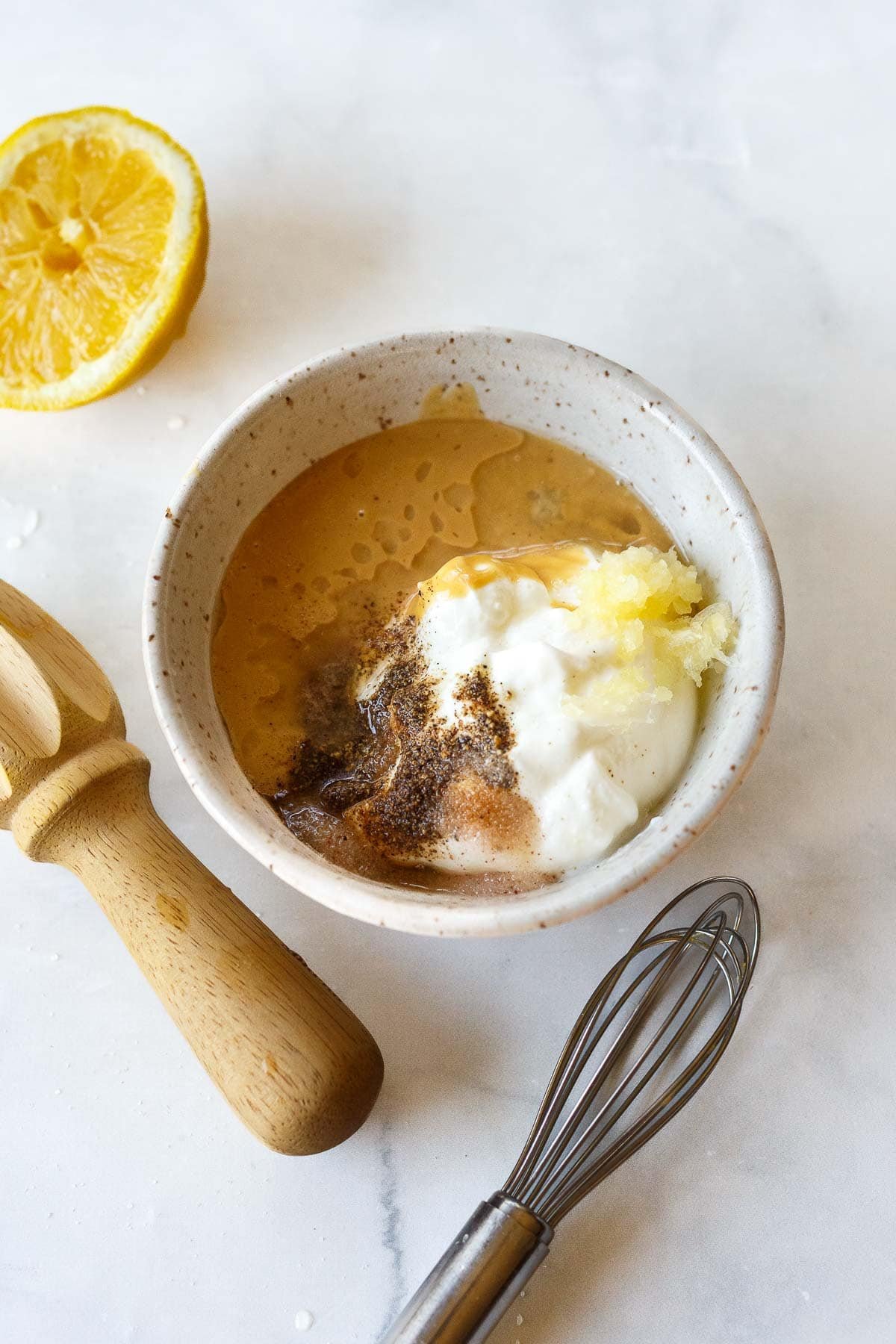 small bowl with tahini, yogurt, lemon juice, garlic, and coriander next to wood juicer and small whisk.