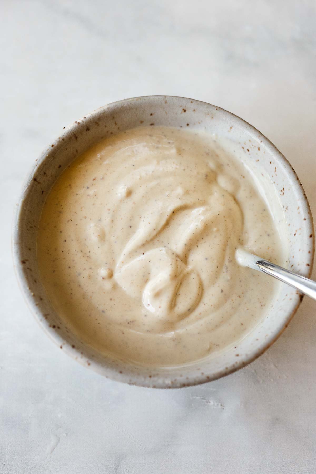small bowl of tahini yogurt dressing with silver spoon.