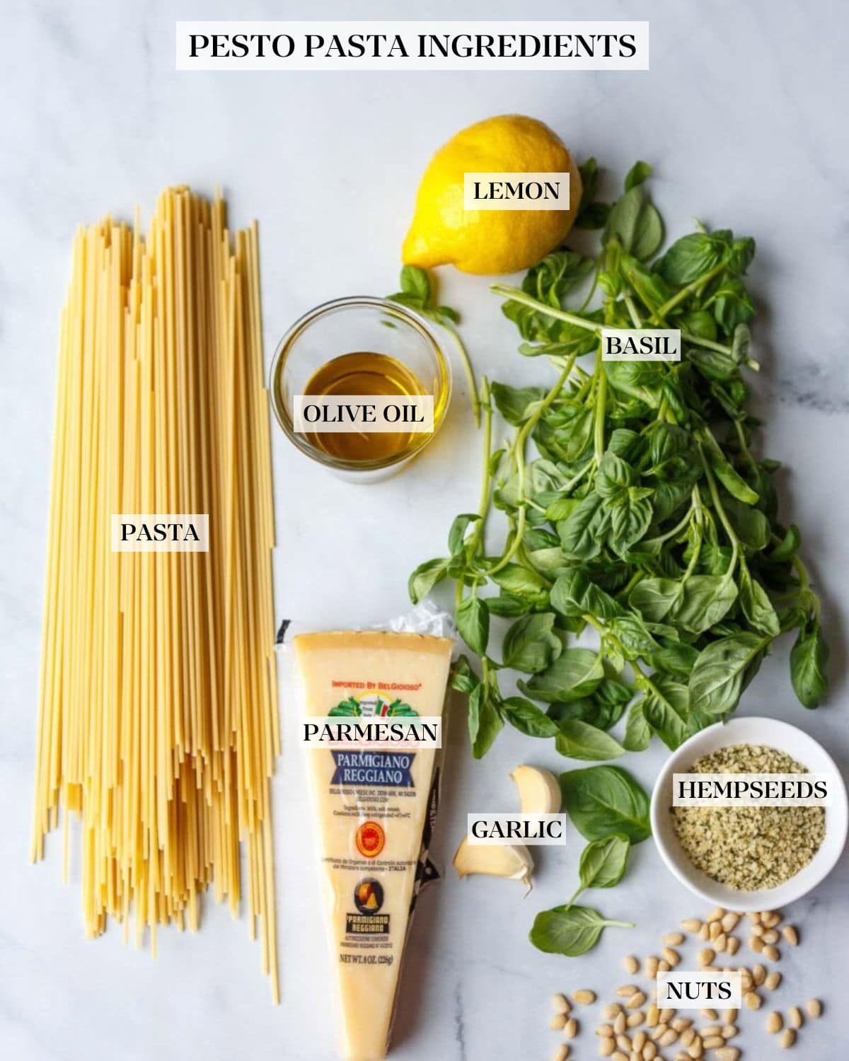 pesto pasta ingredients arranged neatly and labeled - lemon, basil, olive oil, pasta, parmesan, garlic, hemp seeds, and nuts. 