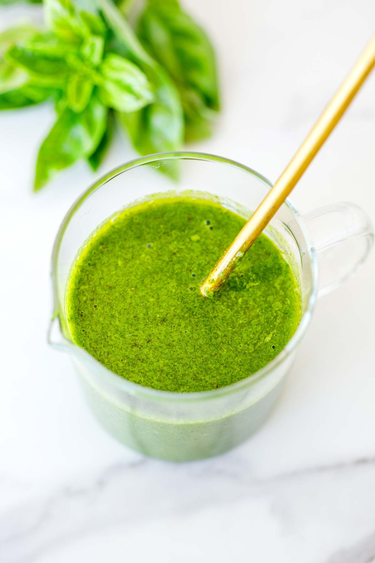 glass jar of basil vinaigrette with gold spoon.