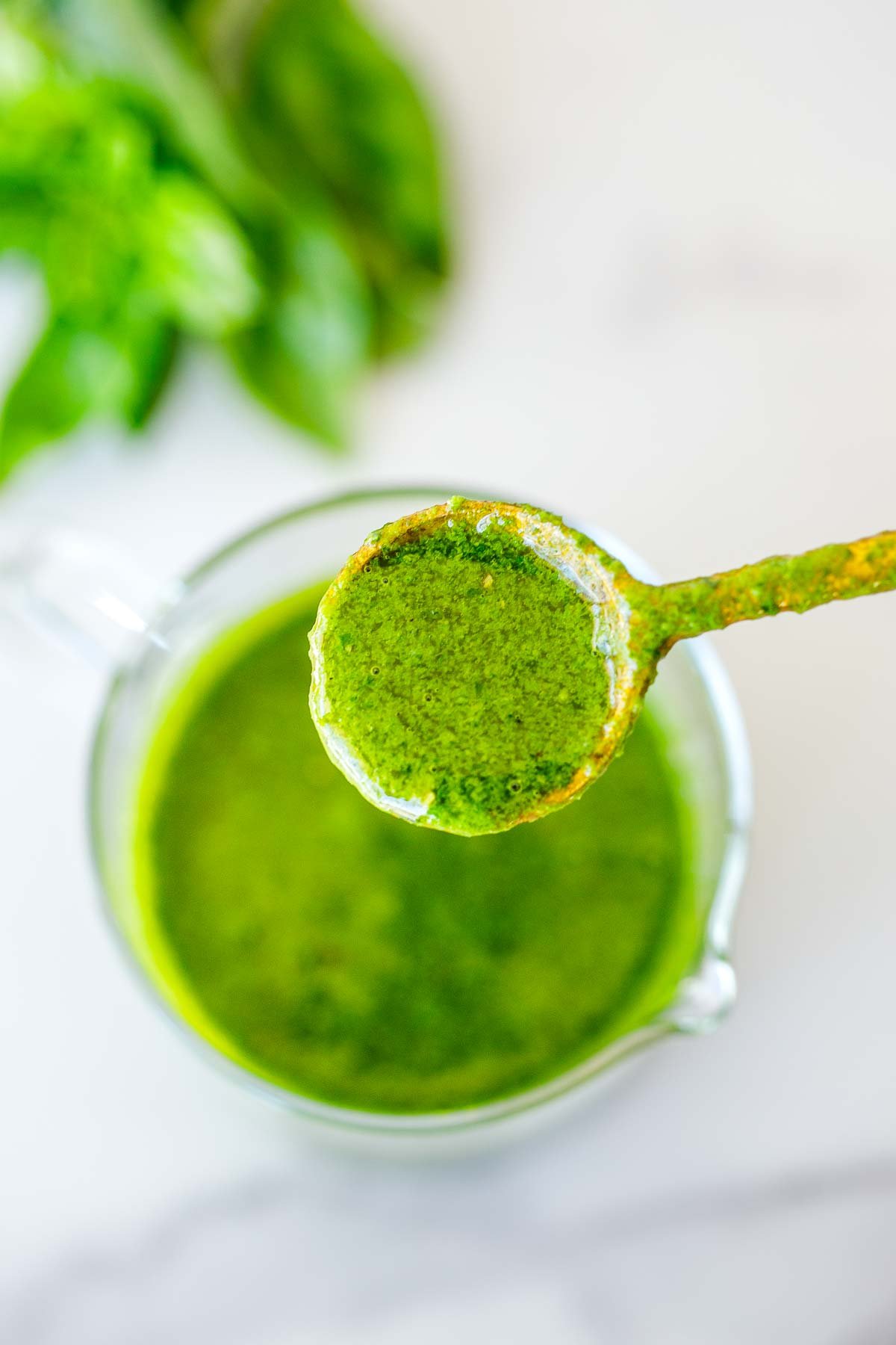 gold spoon holding basil vinaigrette above a glass jar.